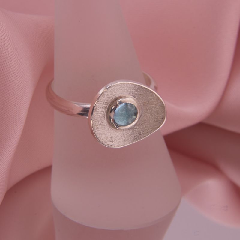 Preview: Präsentation des Rings Isola auf einem Schmuckständer zeigt die skulpturale Form und das Funkeln des blauen Edelsteins.